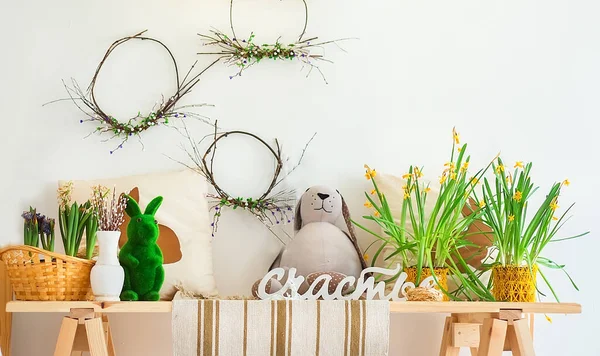 Easter home interior. Vase with pussy-willow twigs with a rabbit, daffodils on the table