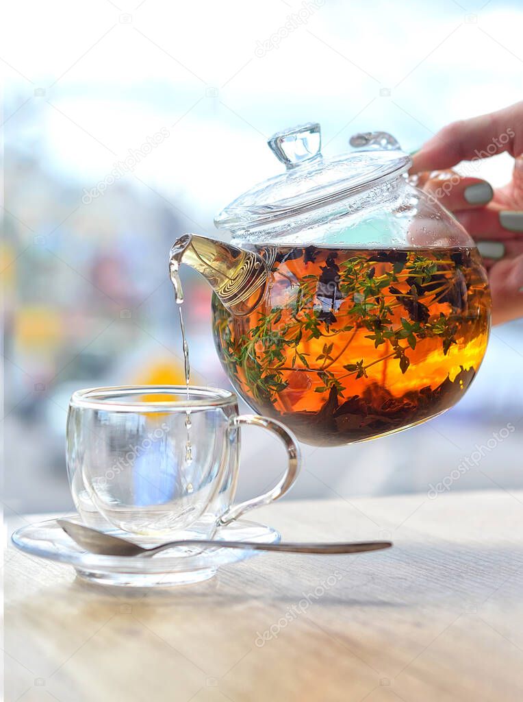 From a glass kettle pour tea into a glass cup on a light background