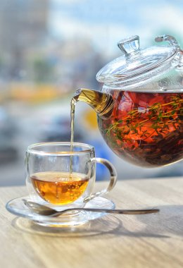 Cam çaydanlıktan cam bir fincana hafif bir arka planda çay dök.