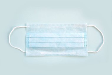 Mavi arka planda lastik kulaklıkları olan mavi proTECTIVE maskesi. Ağız ve burnu örtmek için tipik üç katmanlı cerrahi maske. Bakteri maskesi prosedürü. Koruma kavramı.