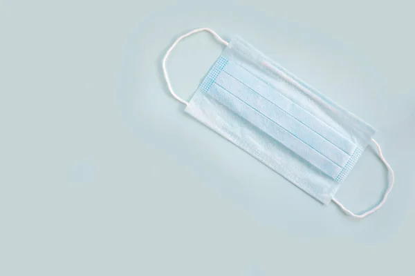 BLUE PROTECTIVE mask with rubber ear straps on a blue background. Typical three-layer surgical mask for covering the mouth and nose. Bacteria mask procedure. Protection concept.