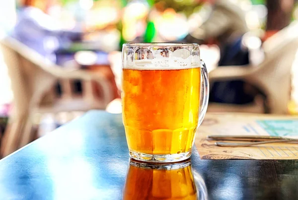 Glass of light beer with foam on a table in the street in summer