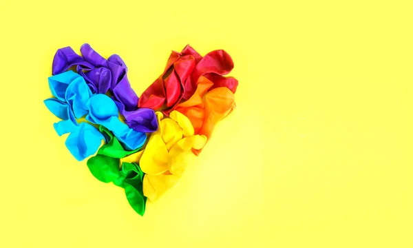 A rainbow heart is a heart out of balloons, like a LGBT pride rainbow flag on a yellow background with copy space. The concept of human rights and freedoms and LGBT people (lesbians, gays, bisexuals)