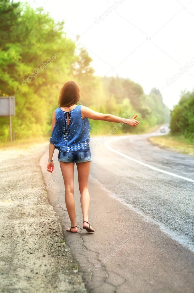 woman hitchhiking on road in forest, hitchhiking with thumbs up in a countryside road, Traveling and hitchhiking concept.