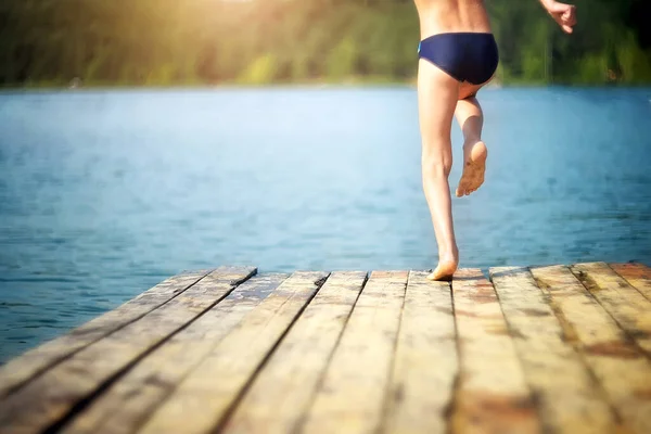 boy jumps from a wooden pier into the water on a blurry summer background. Selective focus