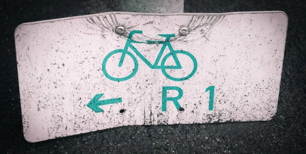 Damaged and weathered bicycle direction sign on the ground — Stock Photo, Image