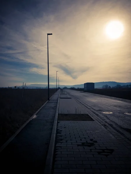 Ländliche Szene einer dunklen Straße mit der Sonne im Hintergrund — Stockfoto