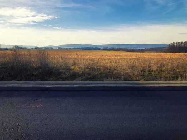 Cena rural de uma estrada em frente a um campo — Fotografia de Stock