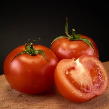 Tahta kesme tahtasındaki kırmızı domatesler, bütün ve siyah arka planda dilimlenmiş, hafif maviyle.