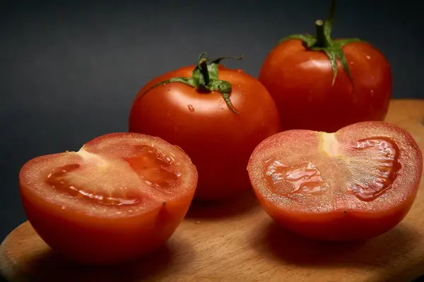 Rote Tomaten auf einem Holzschneidebrett, ganz und in Scheiben geschnitten auf schwarzem Hintergrund, mit leichtem Blu — Stockfoto