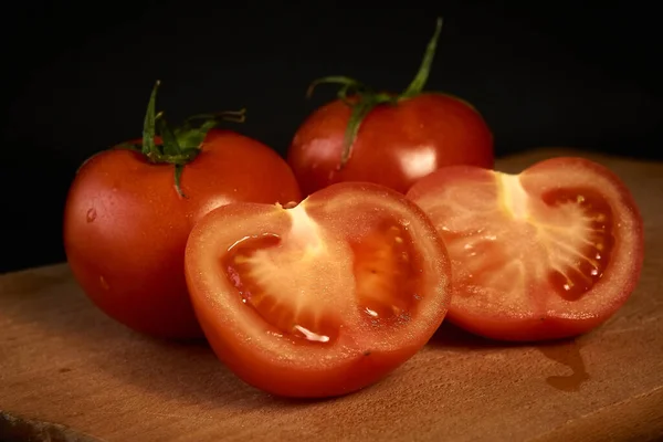 Rote Tomaten auf einem Holzschneidebrett, ganz und in Scheiben geschnitten auf schwarzem Hintergrund, mit leichtem Blu — Stockfoto