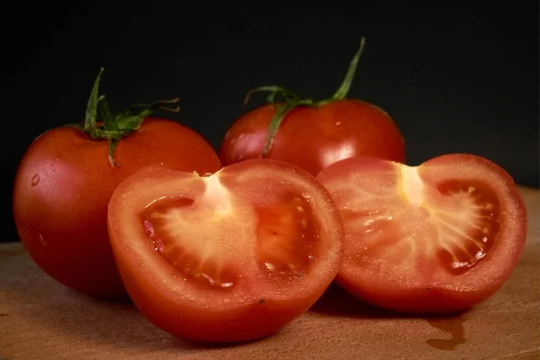 Rote Tomaten auf einem Holzschneidebrett, ganz und in Scheiben geschnitten auf schwarzem Hintergrund, mit leichtem Blu — Stockfoto