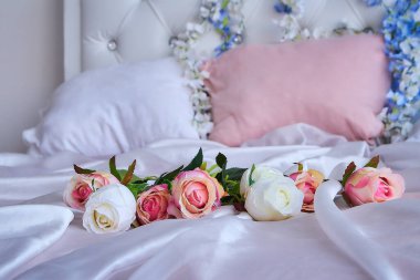Bir buket yapay çiçek büyük bir yatakta beyaz ipek bir battaniyenin üzerinde yatıyor.