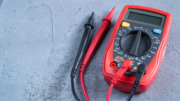 Red multimeter or a multitester, also known as a VOM on gray table. Electronic measuring instrument. Red and black wires