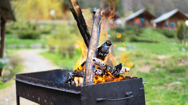 Metal siyah barbekü ve yanan odun ve evin yakınında yeşil arka planda ateş. Barbeküye hazırlanıyorum.