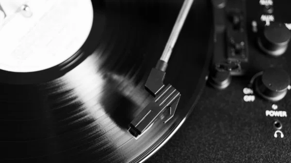 Black and white vinyl needle stylus on rotating black vinyl disk with copy space. Top view of vinyl record player.