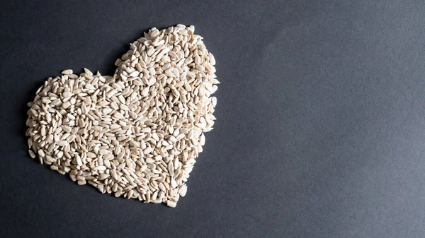 Форма сердца семян подсолнечника на черном фоне с копировальным пространством. Куча семян подсолнечника в форме сердца — стоковое фото