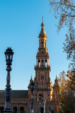 Sevilla 'daki Plaza de Espaa' nın (İspanya 'nın Plaza Meydanı) bir köşesinde bir sokak lambası ve gün batımında bir ağaçla çevrelenmiş bir kule..