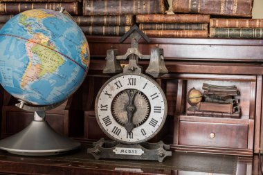 Dünya küresi ve ahşap rafta eski kitapları olan eski bir saat.