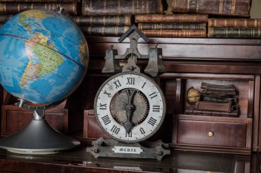 Dünya küresi ve ahşap rafta eski kitapları olan eski bir saat.