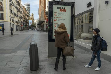 İki yaya, Coronavirus 'un kapatılmasının ardından Madrid' in merkezindeki Preciados Caddesi 'ndeki Coronavirus hakkında bir bilgi işaretine bakıyor.