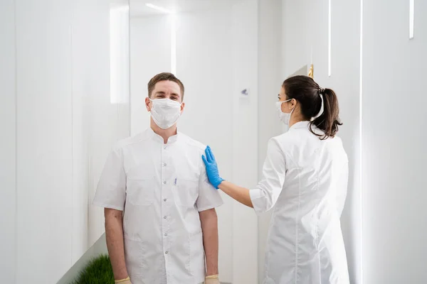 Två glada maskerade läkare en man och en kvinna går i korridoren och ler. Ett modernt sjukhus under pandemin Stockfoto
