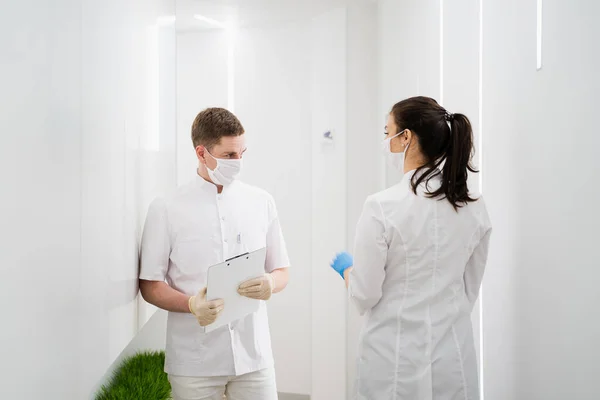 男と女の2人の覆面の医者が廊下を歩く。パンデミックの間の新しい現代病院 ロイヤリティフリーのストック画像