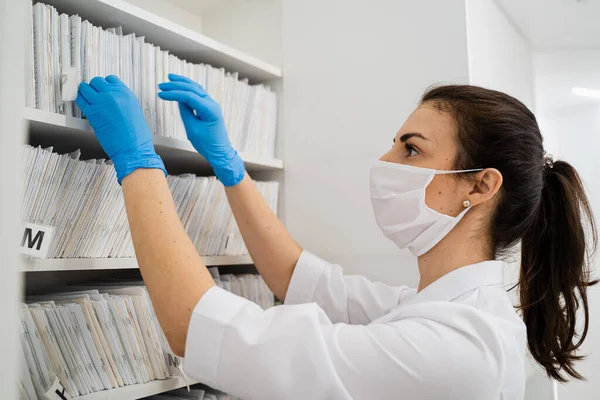 En läkare i mask och vita medicinska kläder söker medicinska dokument i arkivet i den nya moderna kliniken Royaltyfria Stockfoton