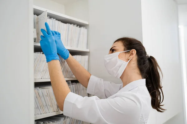 若い覆面の女性医師は、現代病院のアーカイブにケース履歴を読み取ります ストック写真