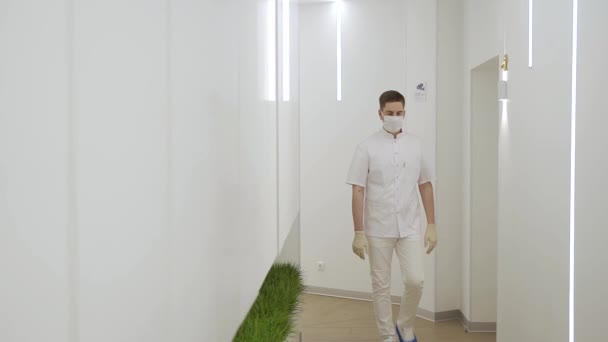 Egy fáradt orvos maszkban és egy fehér orvosi öltönyben sétál végig az új kórház folyosóján, lassítva a mozgást. — Stock videók