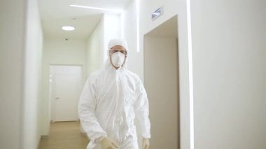 Özel koruyucu kıyafetli, maskeli ve gözlüklü bir doktor salgın sırasında modern bir kliniğin koridorunda hızla yürür.