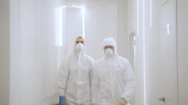 Koruyucu giysili iki doktor, karantina sırasında kırmızı bölgedeki modern bir hastanede yürüyorlar.