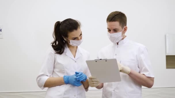 Two masked doctors, a man and a woman, read medical records and discuss the diagnosis — Stock Video