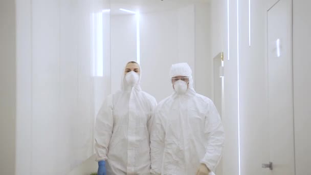 Δύο γιατροί με προστατευτικές στολές περνούν μέσα από ένα σύγχρονο νοσοκομείο στην κόκκινη ζώνη κατά τη διάρκεια της καραντίνας. — Αρχείο Βίντεο