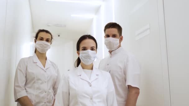 Drie artsen in maskers en medische pakken poseren voor een camera in een modern ziekenhuis — Stockvideo