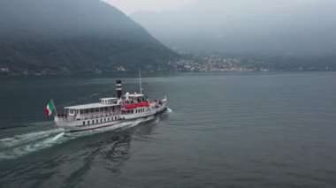Mavi Como Gölü 'ndeki güzel yeşil dağların zemininde yüzen siyah borulu İtalyan beyaz vapurunun havadan görünüşü.