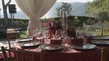 Üzerinde güzel tabaklar, çiçekler, meyveler, şamdanlar olan kırmızı masa örtüsü olan bir festival masası. Como Gölü 'nde bir yaz günü yeşil bir parkın arka planına karşı. Sabit hareket