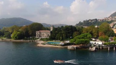 CERNOBBIO, ITALY - 28 Eylül 2019: Villa Erba, havuz, rıhtım, Como Gölü 'nde bir yaz günü sislerin, yeşil ormanların ve İtalyan evlerinin ortasında yelken açan motorlu tekne manzarası