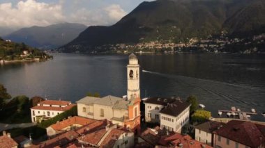 Cernobbio 'daki Saint Vincent Kilisesi' nin hava görüntüsü. Yaz günbatımında bir İHA 'dan panoramik çekim. Bir kuş sürüsü evlerin çatılarında uçuyor.