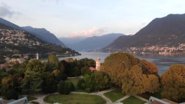 Cernobbio köyünün havadan görünüşü - İtalya 'nın Como Gölü' ndeki güzel bir tatil köyü yeşil ormanlı büyük dağların arka planına karşı. Bir yaz günbatımında İHA 'dan ateş etmek. Martılar kameranın önünde uçar.