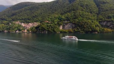 İtalya 'da Como Gölü' nde, yeşil bir dağ olan İtalyan köyünün karşısında beyaz bir zevk gemisinin havadan görünüşü. Bir motorlu tekne buluşmak için acele ediyor. Güneşli bir yaz gününde İHA saldırısı