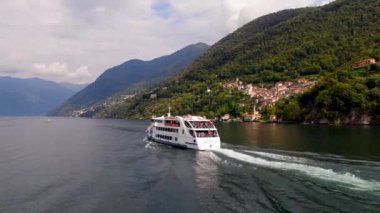COMO, İtalya - 29 Eylül 2019: Orione - suda yüzen ve büyük dalgalar bırakan bir İtalyan modern beyaz feribot. Birçok insan kıçta durup Como Gölü 'nün tadını çıkarıyor. Hava görüntüsü. İHA ateşi