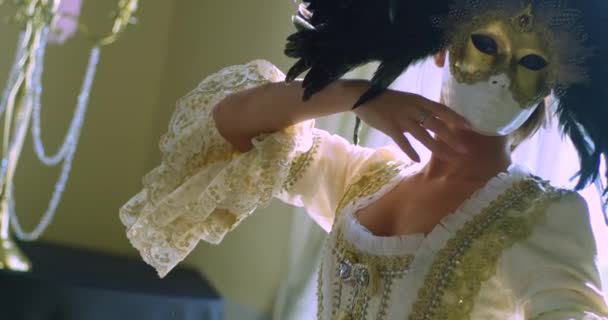 2019年9月26日 一名戴着威尼斯面具 头戴黑色羽毛 身穿金质老式白色连衣裙的女孩在烛台的背景下优雅地挥动着双手 慢动作 — 图库视频影像