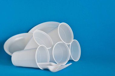 Tek kullanımlık plastik sofra takımı, çatallar, bardaklar, mavi arka planda plakalar. Sorun geri dönüşüm, yeniden kullanım, güvenli gezegen, çevre kavramı. Metin için yer.