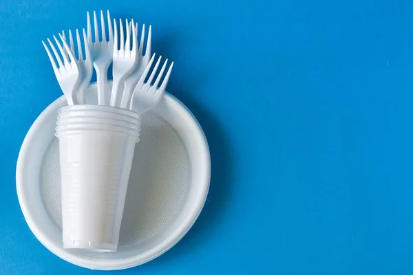 Plastic dishes, disposable tableware, plates, forks, glasses on a blue background. Caring for the environment. The problem is recycling. Reuse. Place for text.