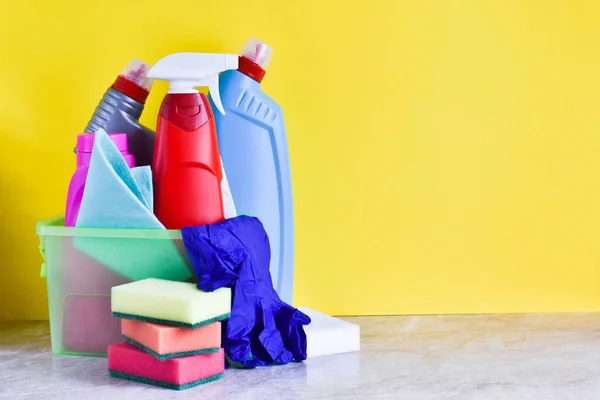 Bottles of detergents and cleaning products on a yellow background. Rags, sponges, gloves, bottles with space for text.