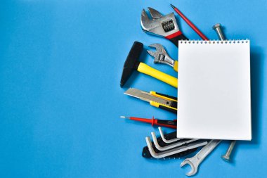 Mavi arka planda tamir için inşaat aletleri. Mesaj için yer. İnşaat ve onarım kavramı. Çekiç, defter, yazı, vida, pense..