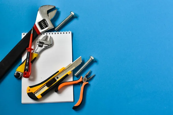 Construction tools for repair on a blue background. Place for text. The concept of construction, repair. Hammer, notebook for writing, screw, pliers.