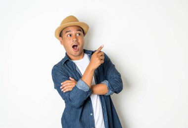 30 yaşındaki mutlu Asyalı adam, şapka takıyor, kot gömlek giyiyor, duruyor, boş bir yeri işaret ediyor..
