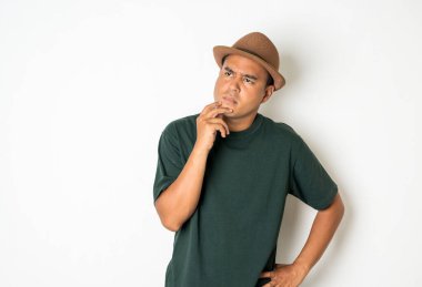 30 yaşlarında Asyalı erkekler şapka giyer, koyu yeşil gömlek giyer. Ciddi bir düşünceyle duruyordu..